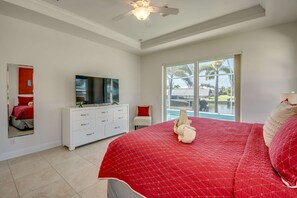 Ein Schlafzimmer mit einem großen Bett, einem Fernseher auf einer weißen Kommode und Blick auf ein Schwimmbad durch eine Glastür.