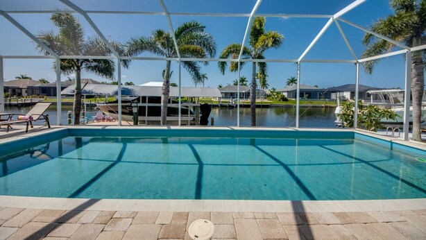 Una piscina con vista despejada al agua, rodeada por una zona cubierta con palmeras y vistas a un cuerpo de agua y edificios al fondo.