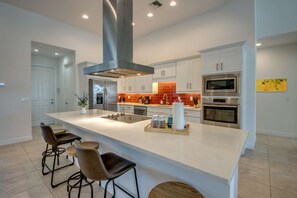 Une cuisine moderne avec des meubles blancs, des appareils en acier inoxydable et un grand îlot central doté de tabourets de bar.