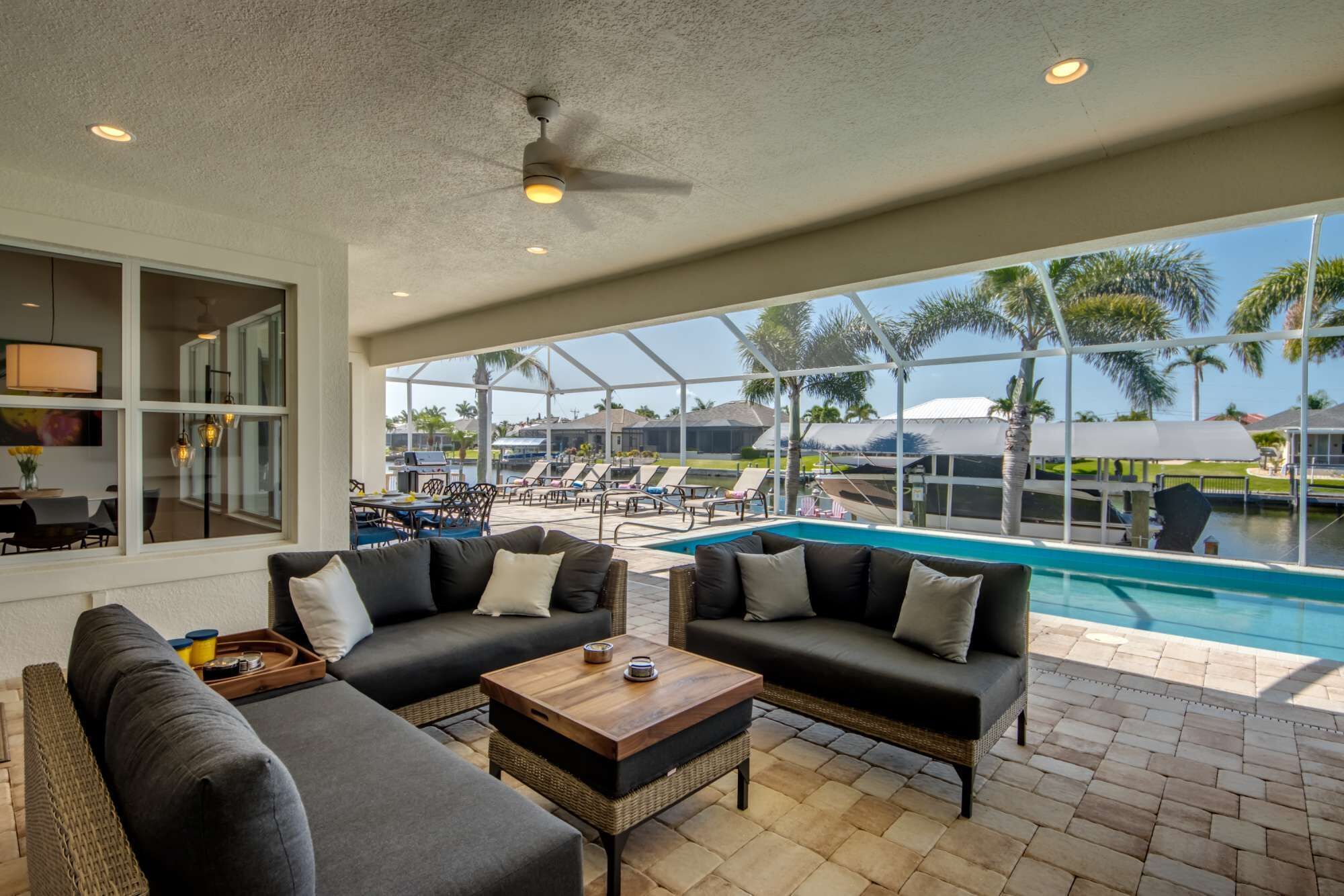 A covered outdoor area with a pool, lounge chairs, and a seating area with sofas and a coffee table.
