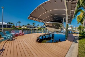 Ein Boot liegt in einer Marina festgemacht, mit einem überdachten Deck, Stühlen und Blick auf Wasser und Gebäude im Hintergrund.