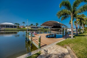 Un puerto deportivo con un muelle techado para barcos, un paseo marítimo de madera y palmeras.