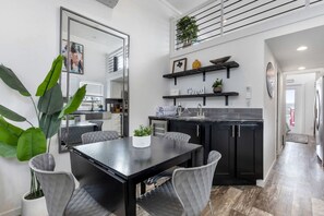 A modern kitchen with dark cabinetry, a black countertop, and a dining area with a black table and grey upholstered chairs. - Bright Tiny Home Escape with Resort Amenities Near Fredericksburg, TX (Fredericksburg)