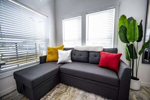 A sectional sofa with a grey fabric, three cushions in yellow, white, and red, and a large green plant beside it. - Bright Tiny Home Escape with Resort Amenities Near Fredericksburg, TX (Fredericksburg)
