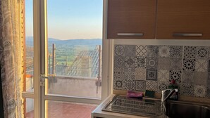 A kitchen with a view of a balcony, a tiled backsplash, and wooden cabinets. - Luce, Penthouse with Panoramic Terrace (Assisi)