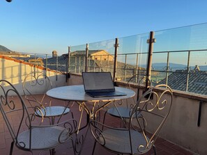 A balcony with a table and chairs, a laptop, and a view of buildings and hills. - Vrbo Property (Assisi)