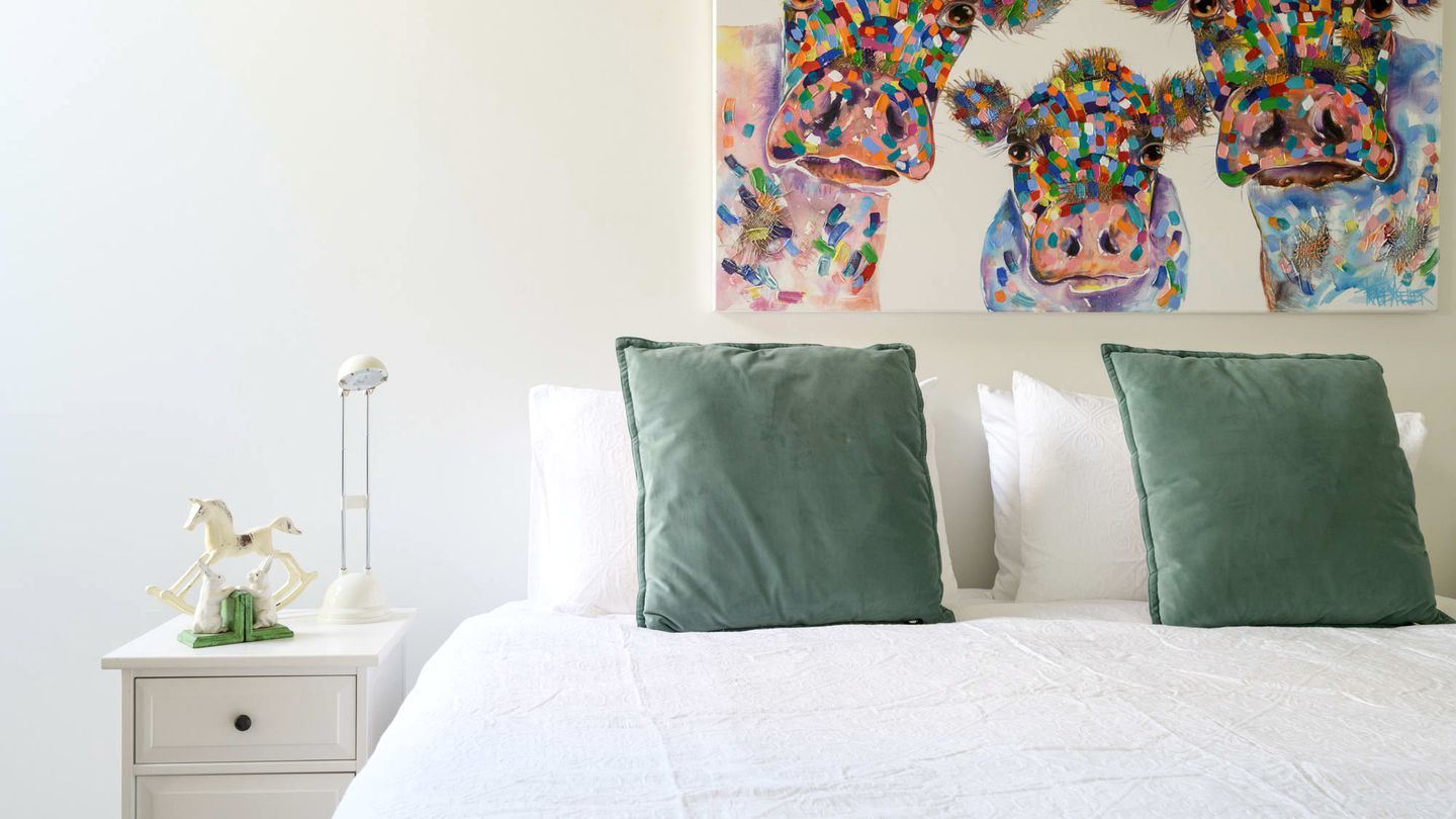 Une chambre à coucher avec un lit, des oreillers, une table de chevet, une lampe et un tableau au mur.
