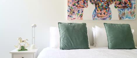 Une chambre à coucher avec un lit, des oreillers, une table de chevet, une lampe et un tableau au mur.