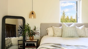 A bedroom with a bed, a mirror, a hanging light, a window, and a plant.