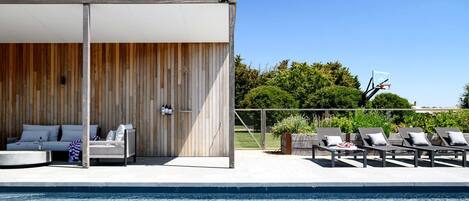 A poolside area with a covered seating area, lounge chairs, and a basketball hoop.