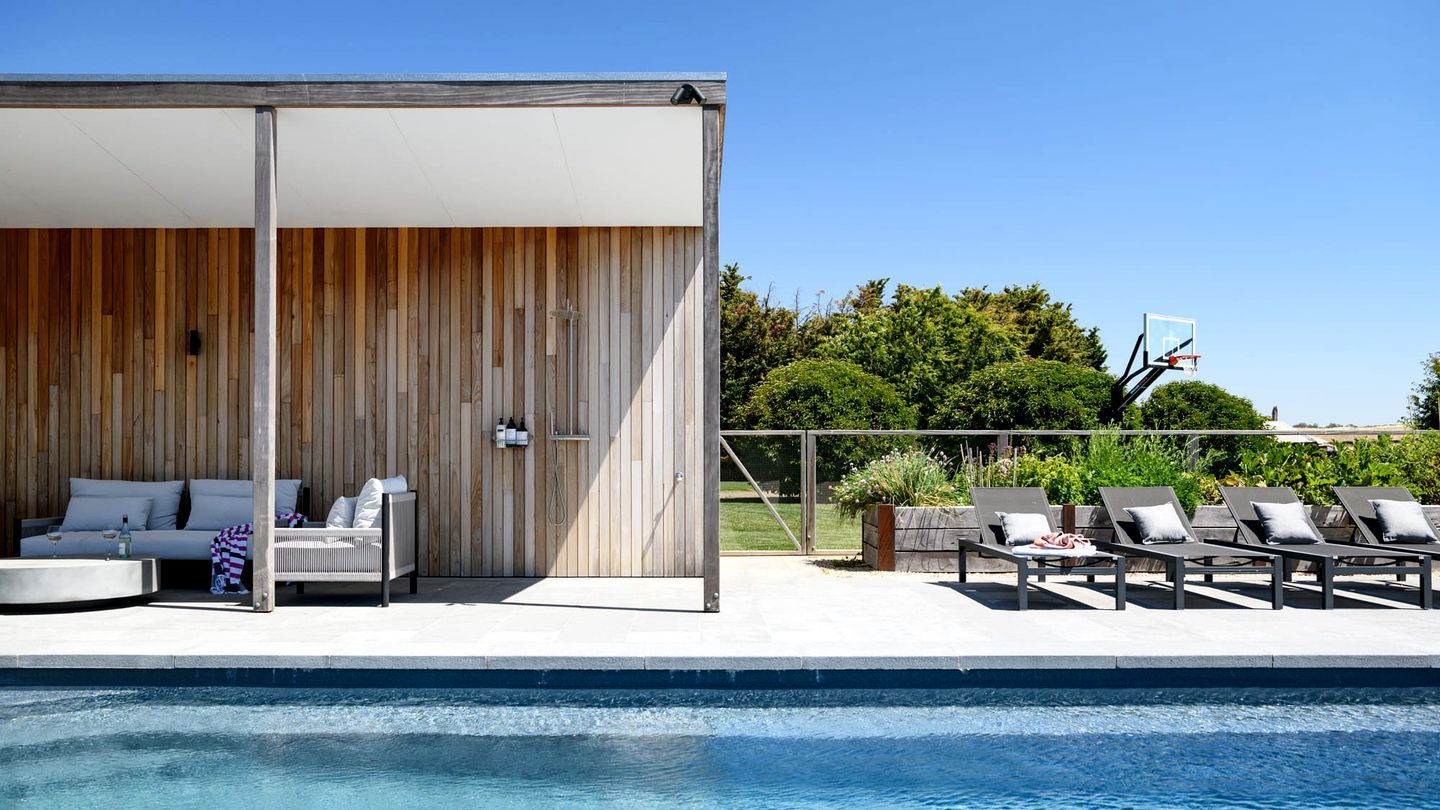 A poolside area with a covered seating area, lounge chairs, and a basketball hoop.