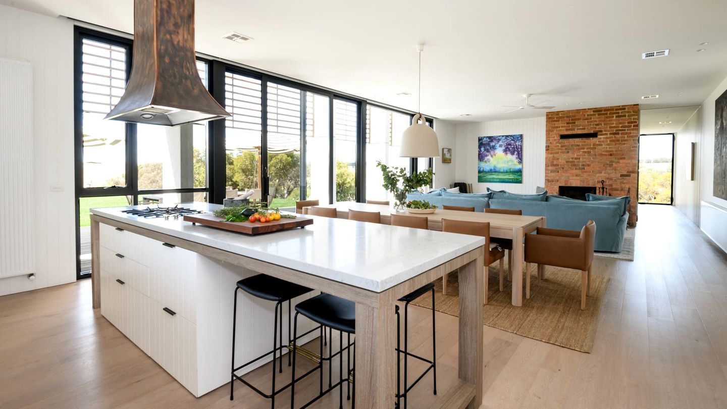A modern kitchen with a large island, dining area with a blue sofa, and a brick fireplace.
