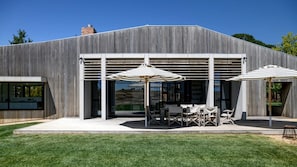 A modern building with a covered patio area featuring outdoor furniture and umbrellas.