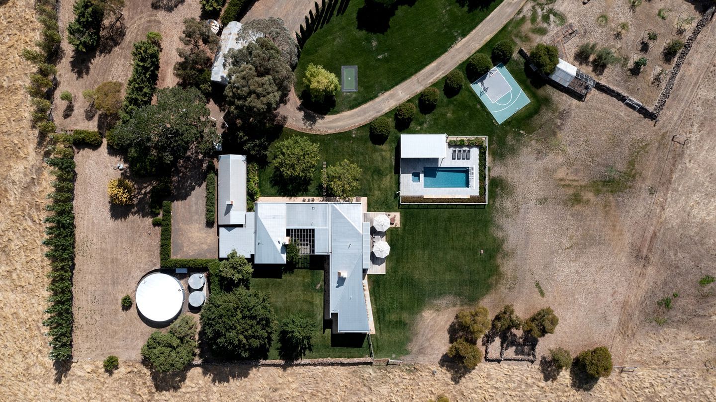 An aerial view of a property with a swimming pool, a tennis court, and a large house with a garage.