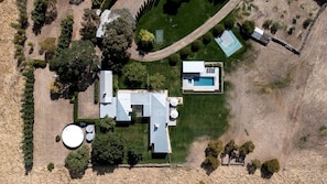 An aerial view of a property with a swimming pool, a tennis court, and a large house with a garage.