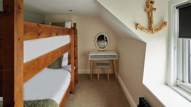 Een slaapkamer met een stapelbed, een bureau met spiegel en een raam.