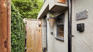 Een smalle steeg met een houten poort, een bloembak met bloemen, en een gebouw met een bord waarop '21 THE FRONT' staat.