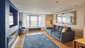 Een woonkamer met een blauwe bank, een grote spiegel en uitzicht op de omgeving door een raam.
