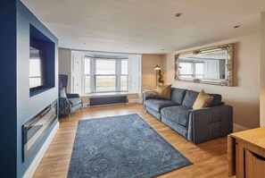 A living room with a blue sofa, a large mirror, and a view of the outdoors through a window. - Host & Stay - Captain's Quarters (Seaton Carew)