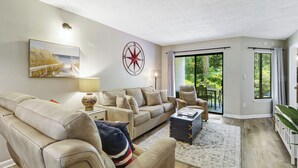 A living room with a sofa, armchairs, a coffee table, a lamp, a painting, a compass wall decoration, and a sliding glass door leading to a balcony. - Ocean Oriented Oasis!  Indoor Heated Pool!  Pickleball! Hot Tub! (Hilton Head)