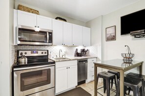 A modern kitchen with white cabinets, a stainless steel microwave, an oven, a dishwasher, and a small dining area with stools. - Ocean Oriented Oasis!  Indoor Heated Pool!  Pickleball! Hot Tub! (Hilton Head)