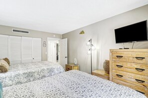 A bedroom with two beds, a dresser, a television, and a door leading to another room. - Ocean Oriented Oasis!  Indoor Heated Pool!  Pickleball! Hot Tub! (Hilton Head)