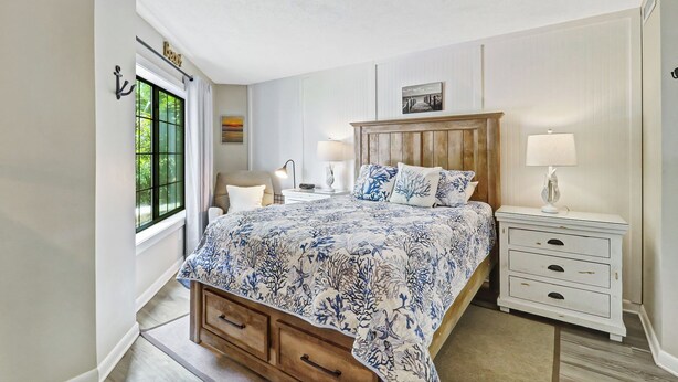 A bedroom with a bed, bedside tables, a chair, and a window with curtains. - Ocean Oriented Oasis!  Indoor Heated Pool!  Pickleball! Hot Tub! (Hilton Head)