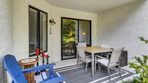 A patio with a table and chairs, a blue chair, and a small wooden table with candles. - Ocean Oriented Oasis!  Indoor Heated Pool!  Pickleball! Hot Tub! (Hilton Head)