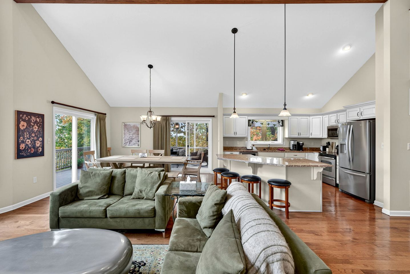 A spacious living area with a large green sofa, a dining table, and a kitchen with white cabinets and stainless steel appliances.