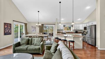 A spacious living area with a large green sofa, a dining table, and a kitchen with white cabinets and stainless steel appliances.