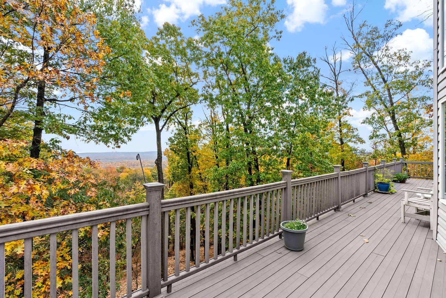 A wooden deck with a railing, overlooking a forested area with autumn foliage.