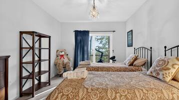 A bedroom with two beds, a large teddy bear, a chandelier, and a view of the outdoors.