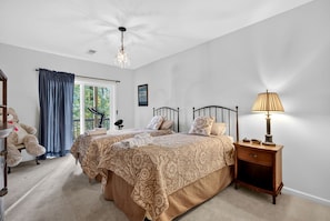 A bedroom with two beds, a nightstand, a lamp, a large teddy bear, and a view of the outdoors through a window. - Scenic Dog-Friendly Mountain Chalet with Panoramic Views & Game Loft Near Berkeley Springs, Hedgesville, WV (Hedgesville)
