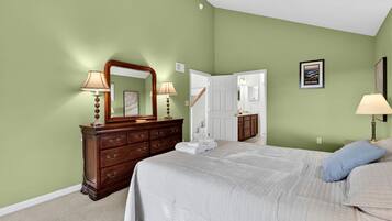 A bedroom with a large bed, a dresser with a mirror, and a door leading to a bathroom.