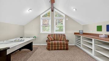 A room with a pool table, a plaid armchair, and a ceiling fan.
