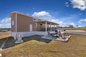Ein Bungalow mit überdachter Veranda, einer kleinen Sitzgruppe im Freien mit Stühlen und Tisch sowie einem gepflegten Rasen.