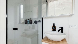 Un baño moderno con cabina de ducha de vidrio, un lavamanos blanco con encimera de madera y un espejo sobre el lavamanos.