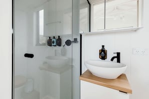 A modern bathroom with a glass shower enclosure, a white sink with a wooden countertop, and a mirror above the sink. - Reconnect with Nature at this Fabulous Tiny Home in Queensland (Coalbank)