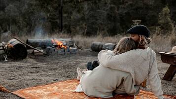 Two people sitting on a blanket outdoors with a campfire in the background.