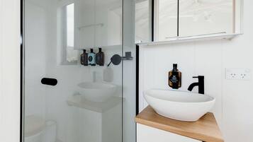 Ein modernes Badezimmer mit Duschkabine aus Glas, einem weißen Waschbecken mit Holzablage und einem Spiegel über dem Waschbecken.