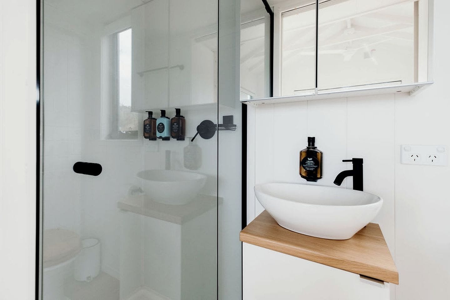 Ein modernes Badezimmer mit Duschkabine aus Glas, einem weißen Waschbecken mit Holzablage und einem Spiegel über dem Waschbecken.