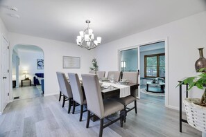 A dining area with a chandelier, a table set for four, and a view through a glass door. - Sandlewood Getaway  Fire Pit  Pool  Hot Tub (East Stroudsburg)