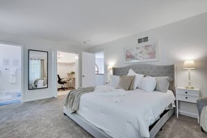 A bedroom with a large bed, bedside tables, a nightstand, a mirror, and a door leading to another room. - Sandlewood Getaway  Fire Pit  Pool  Hot Tub (East Stroudsburg)