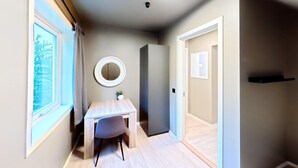 A narrow hallway with a wooden desk, a round mirror, and a small plant.