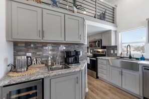 A modern kitchen with grey cabinets, a granite countertop, a coffee maker, and a stainless steel sink. - Charming Tiny Home Retreat with Resort-Style Pool Near Fredericksburg, TX (Fredericksburg)