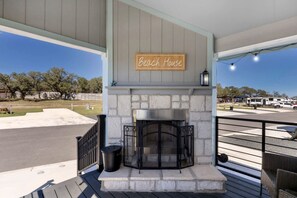 A covered outdoor area with a stone fireplace, a sign reading 'Bench House,' and a view of a parking lot and RVs. - Charming Tiny Home Retreat with Resort-Style Pool Near Fredericksburg, TX (Fredericksburg)