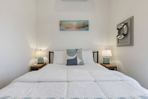 A neatly made bed with white bedding, two bedside lamps, a painting above the bed, and a welcome sign on the wall. - Charming Tiny Home Retreat with Resort-Style Pool Near Fredericksburg, TX (Fredericksburg)