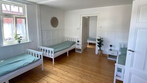 A room with two single beds, a wooden floor, a window, and a door.