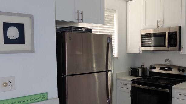A modern kitchen with stainless steel appliances, white cabinetry, and a tiled backsplash. - 2-Min Walk to Beach · 1BR Duplex w/ Private Lot (Redington Shores)