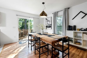 Zona pranzo con tavolo in legno, sedie nere, lampadario e libreria con libri e oggetti decorativi.